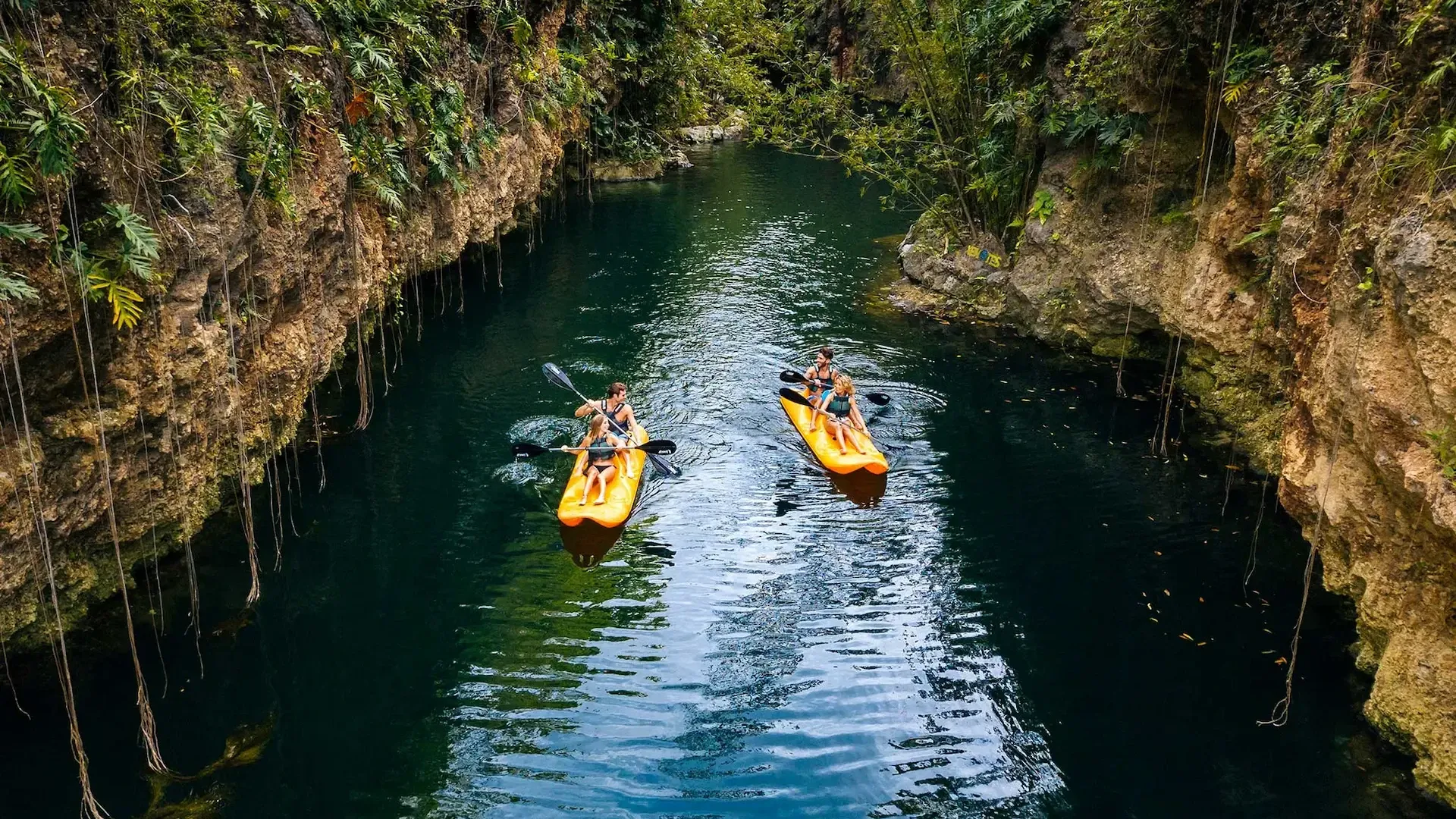 Visitantes recorriendo en kayak un cenote abierto rodeado de paredes rocosas y vegetación