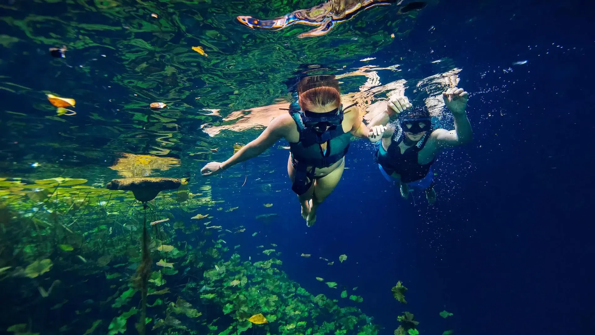 Dos visitantes con chaleco salvavidas realizando nado de exploración en un cenote