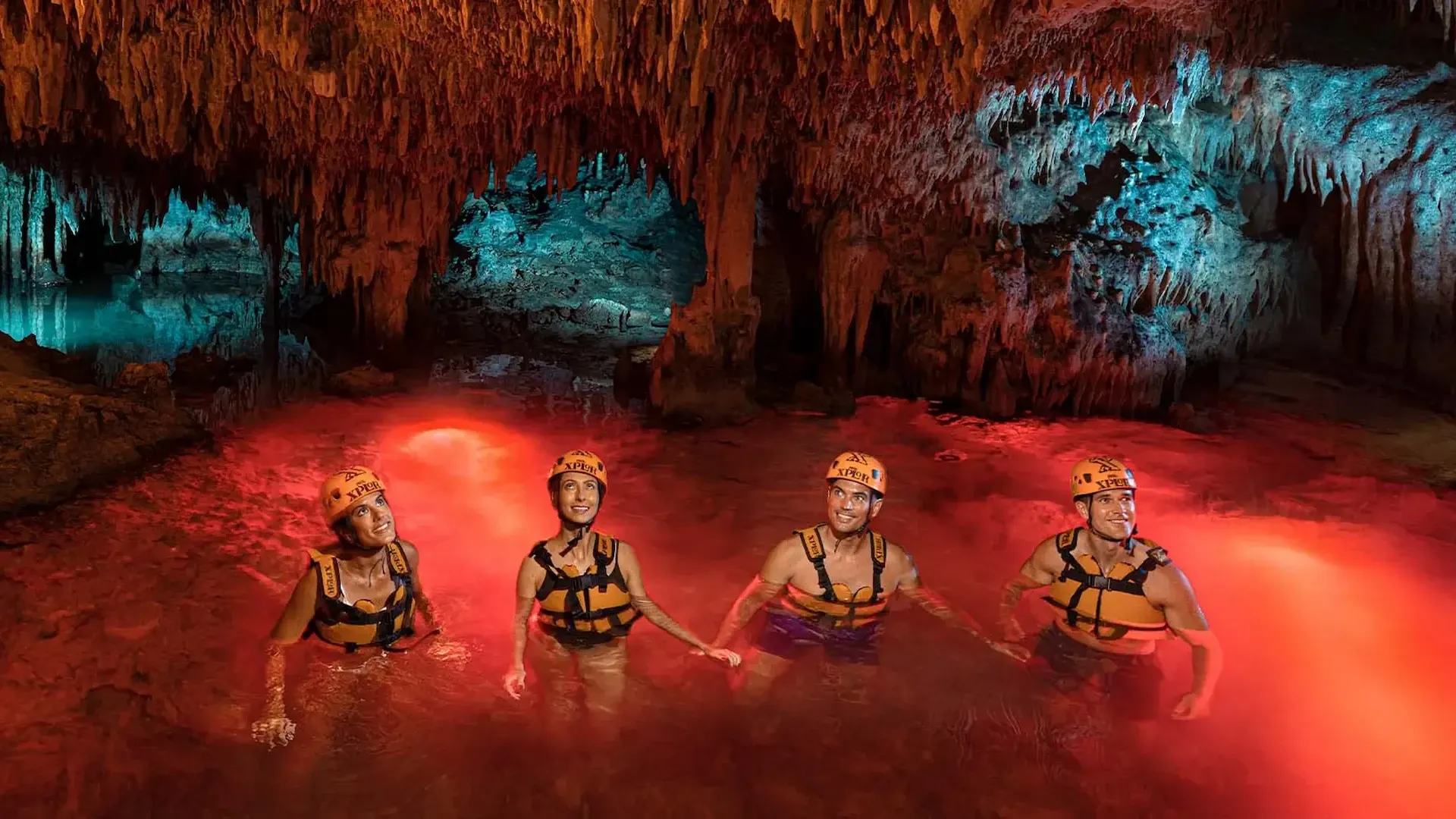 Cuatro visitantes nadando en un río subterráneo iluminado durante Xplor Fuego