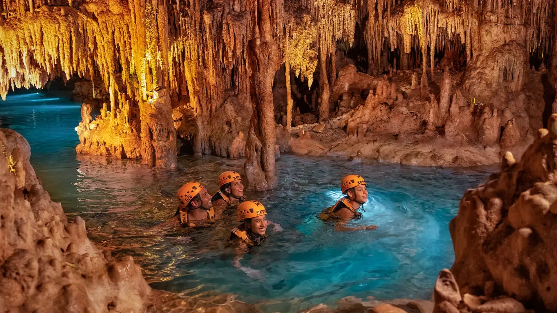 Visitantes nadando en un río subterráneo entre estalactitas en Xplor