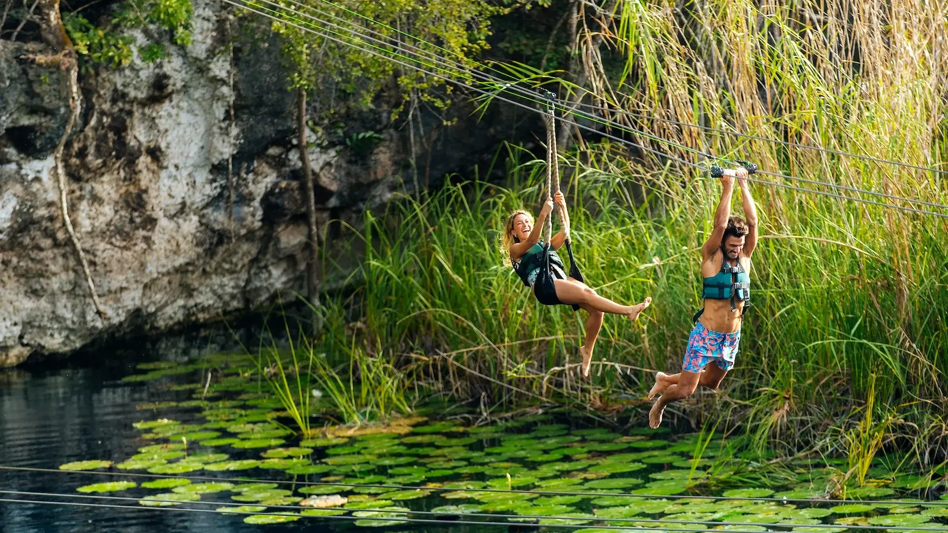 Dos visitantes deslizándose en tirolesa sobre el agua de un cenote abierto