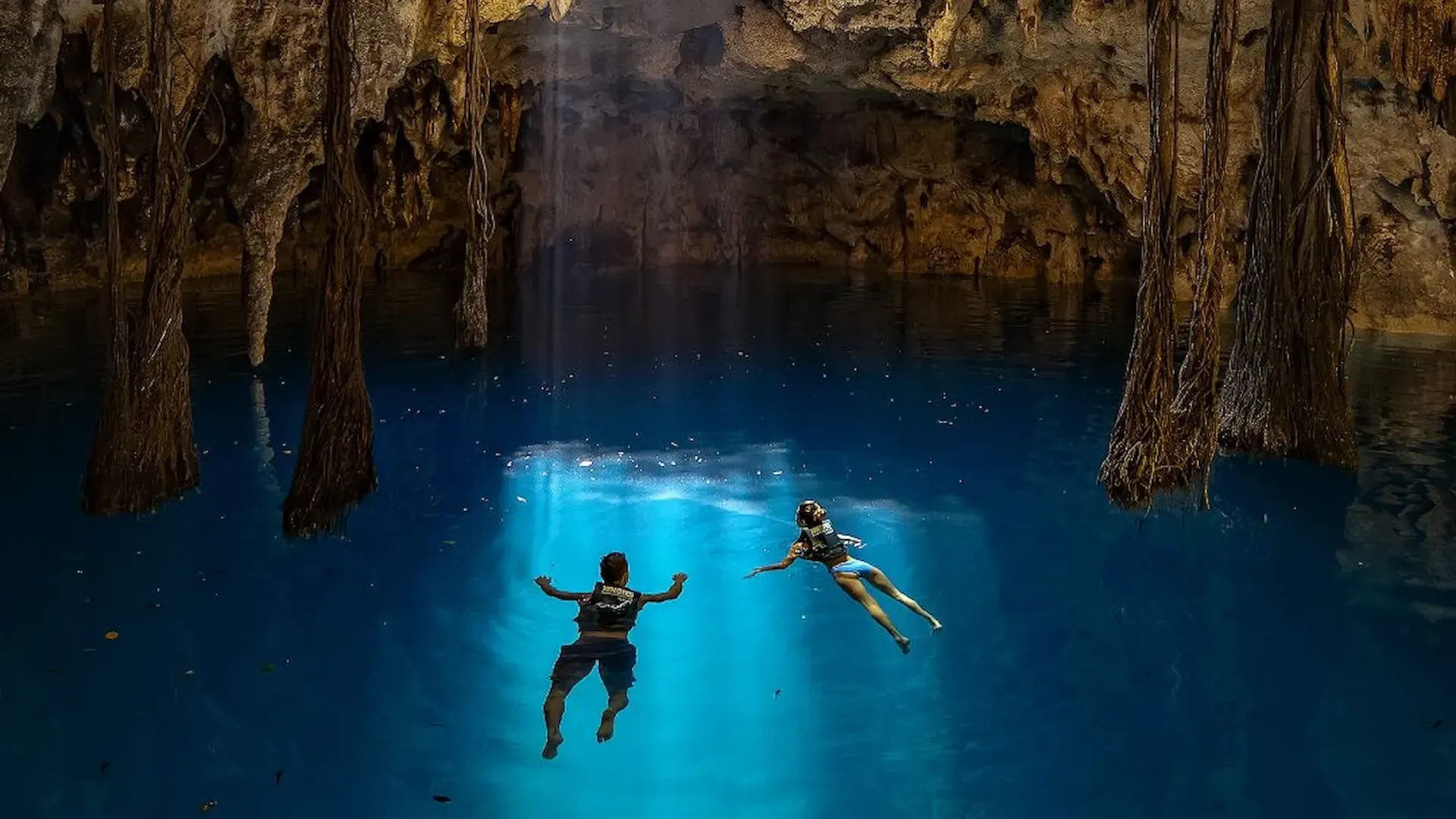 Visitantes nadando en el interior de un cenote de caverna iluminado por una abertura natural