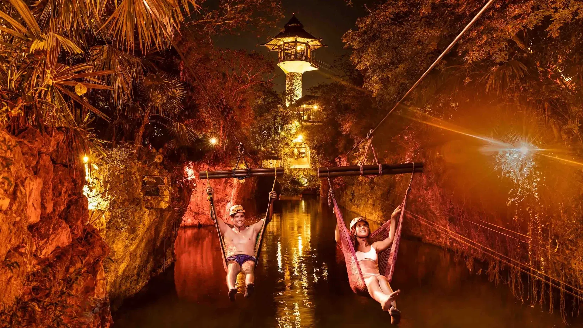 Pareja descendiendo en hamacas hacia el agua durante el Hamacuatizaje de Xplor Fuego